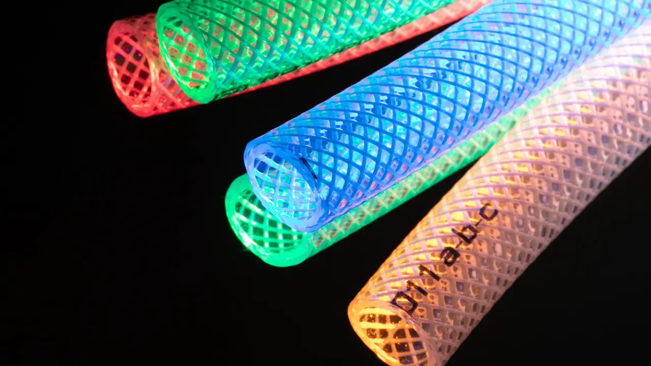 Mangueras trenzadas translúcidas iluminadas en rojo, verde, azul y naranja sobre fondo negro